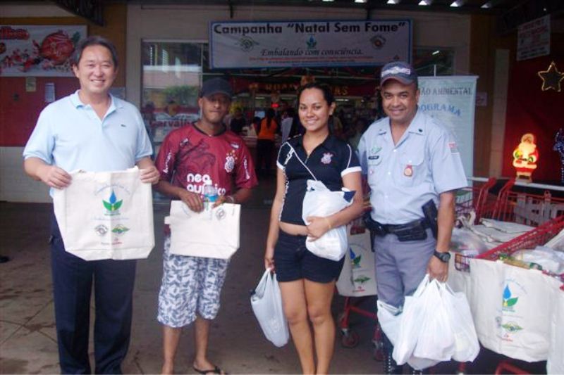 A foto destaca o Prefeito Arnaldo Enomoto, o Sargento Roberto da Policia Militar Ambiental e clientes do Supermercado Carvalho durante a troca de sacolas por alimentos.